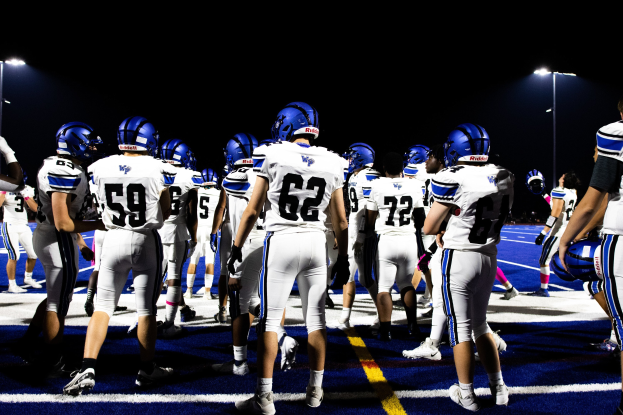 Eine Gruppe von Fußballspielern in Helmen und Stiefeln, die auf einem Feld unter Flutlicht stehen und bereit zum Spiel zu sein scheinen.