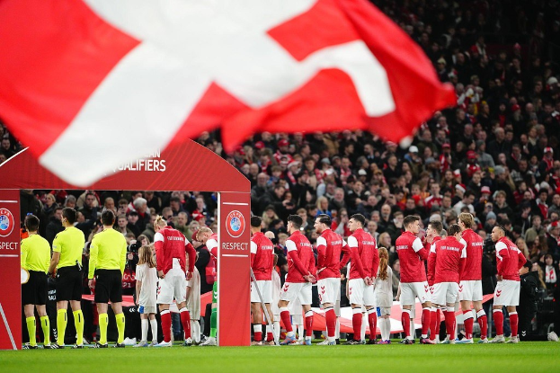Eine Gruppe von Menschen auf einem Fußballfeld mit einer roten und weißen Flagge im Vordergrund, einem Bogen mit der Aufschrift "Bayern Munich vs Bayern Munich Betting Tips & Preview" im Hintergrund und einer großen Menge im Stadion.