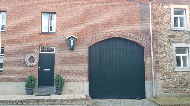 Ziegelgebäude mit grüner Tür und Fenstern, einem Rohr an der Seite und Topfpflanzen davor.