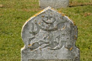 Grabstein mit arabischer Inschrift in einem grasbewachsenen Friedhof.