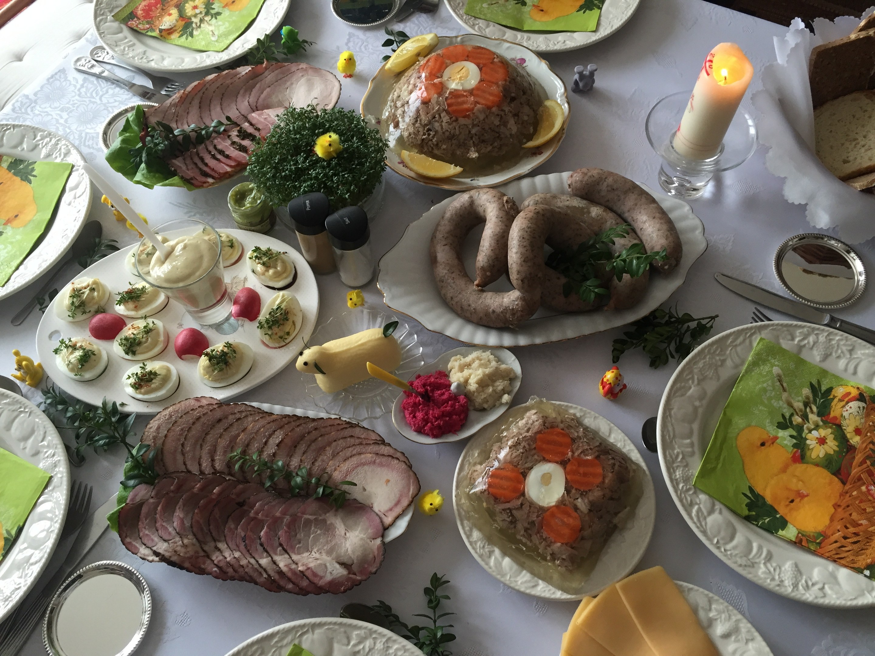 Ein langer Tisch mit einer Vielzahl von Gerichten, Geschirr und Kerzen, umgeben von Stühlen, der ein traditionelles deutsches Osteressen darstellt.