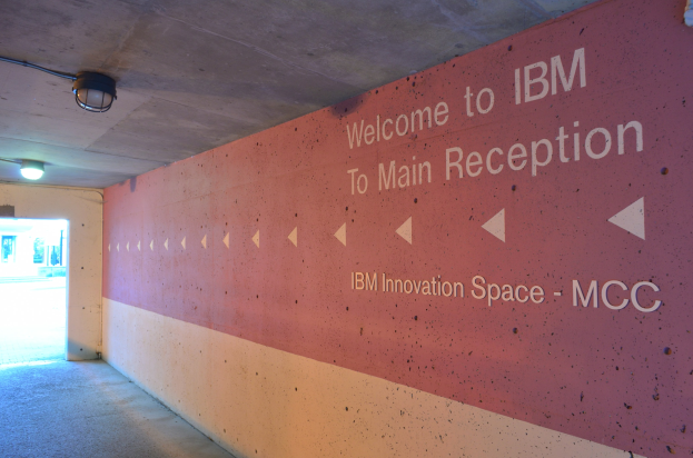 Eine Wand mit den Worten "Willkommen bei IBM" beleuchtet von Deckenlampen, mit einer Tür im Hintergrund beschriftet mit "IBM Innovation Space MCC".