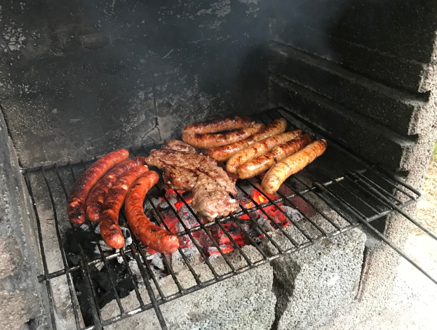 Grill mit Würstchen und Fleisch auf Kohle und Feuer, im Freien auf Gras.