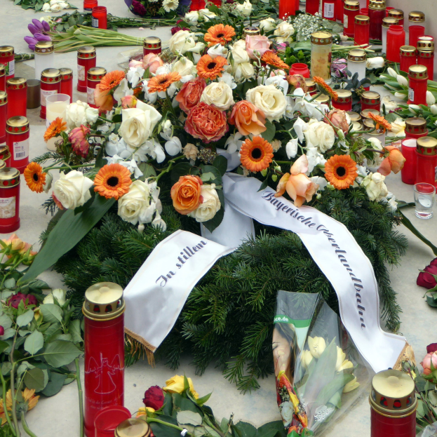 Mahnmal in Berlin mit Blumen und Kerzen, die auf dem Boden vor einer Wand aufgestellt sind.