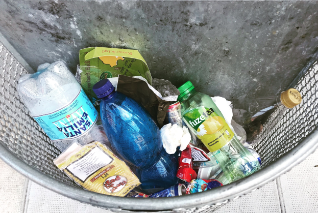 Ein Metallmüllcontainer voller verschiedener Plastikflaschen, Tüten und anderer weggeworfener Gegenstände.
