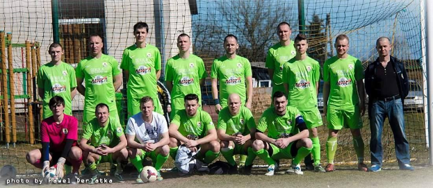 Gruppe von Männern in grünen T-Shirts, die auf einem Fußballfeld stehen und knien, mit einem Ball vor ihnen.