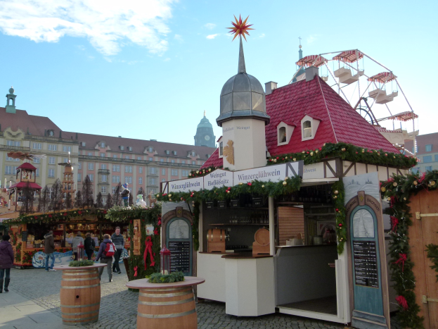 Ein geschäftiger Weihnachtsmarkt in Nürnberg, Deutschland, mit Menschen um geschmückte Stände, festliche Lichter, ein Riesenrad, Gebäude und eine Tafel mit Schrift auf der rechten Seite.