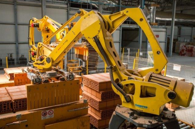 Industrielles Lager mit gestapelten Kisten, Kränen, Zaun, Pfählen und einer fernen Wand in einer Fertigungsumgebung.