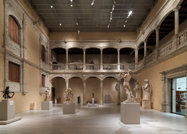 Großer Raum in einem Museum mit zahlreichen Statuen und Skulpturen auf Sockeln, architektonischen Elementen einschließlich Wänden, Säulen, Geländern und einer Decke mit Beleuchtung, mit wenigen Menschen.