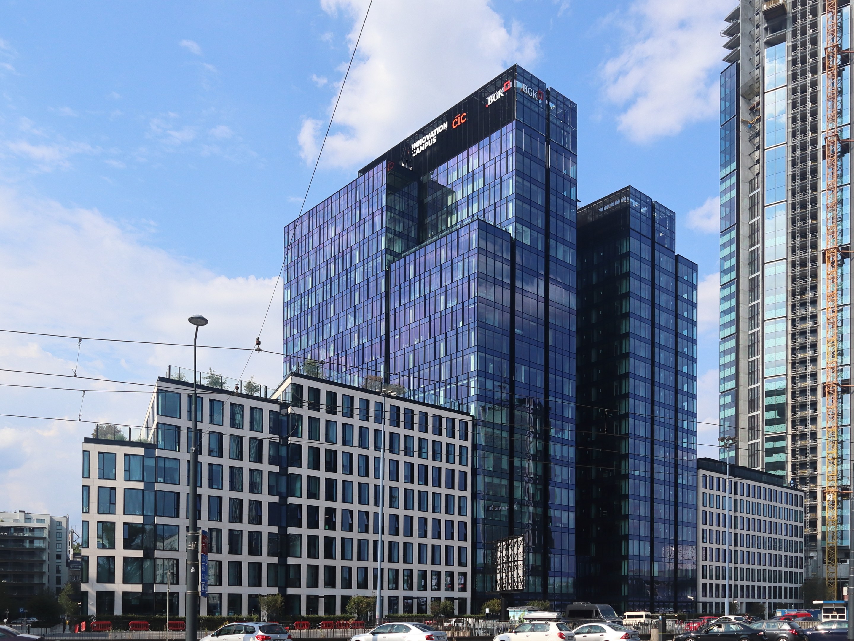 Großes Gebäude mit vielen Fenstern, die Deutsche Bank Hauptverwaltung in Frankfurt, Deutschland, umgeben von städtischen Elementen einschließlich Straßenlaternen, Lichtern, Fahrzeugen, Grünflächen und einem bewölkten Himmel.