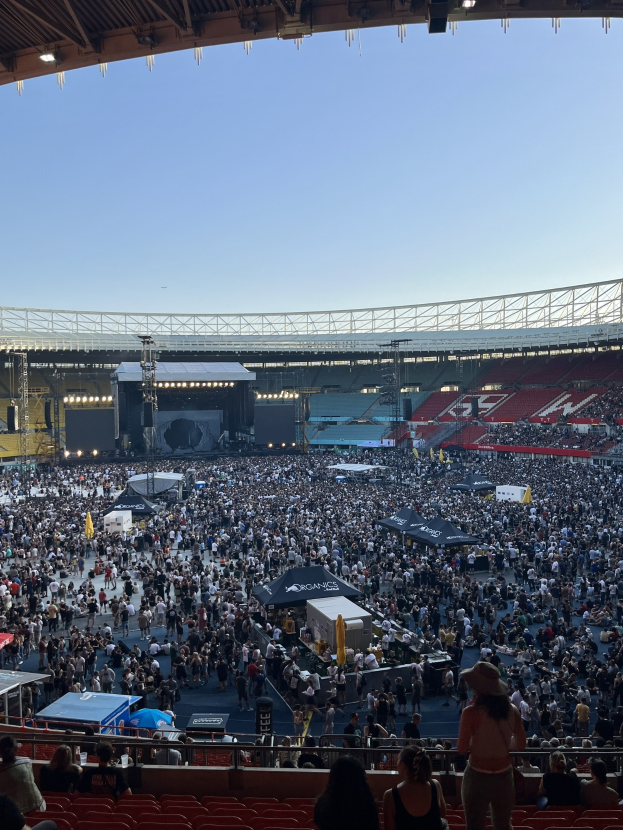 Große Menschenmenge auf Tribünen und im Stehen in einem Stadion mit Zelten, Geländern und Beleuchtung von oben, was auf ein Konzert in der O2 Arena in London hindeutet.