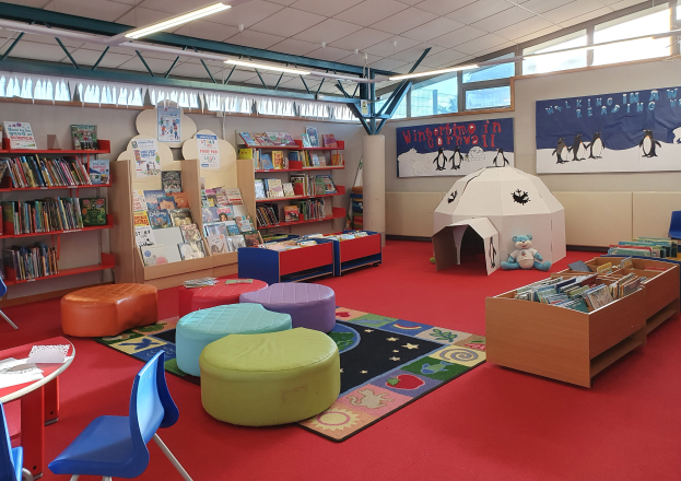Eine Kinderbibliothek voller Bücher, Möbel, Lehrtafeln und natürlichem Licht von großen Fenstern.