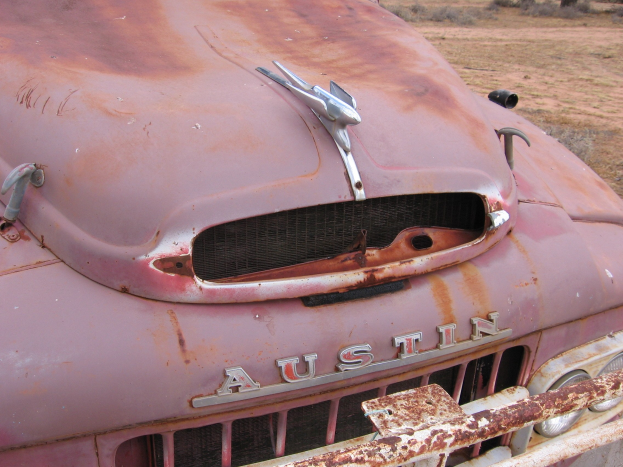 Ein alter, rostiger Lastwagen auf einem Feld mit Bäumen und einem klaren blauen Himmel im Hintergrund.