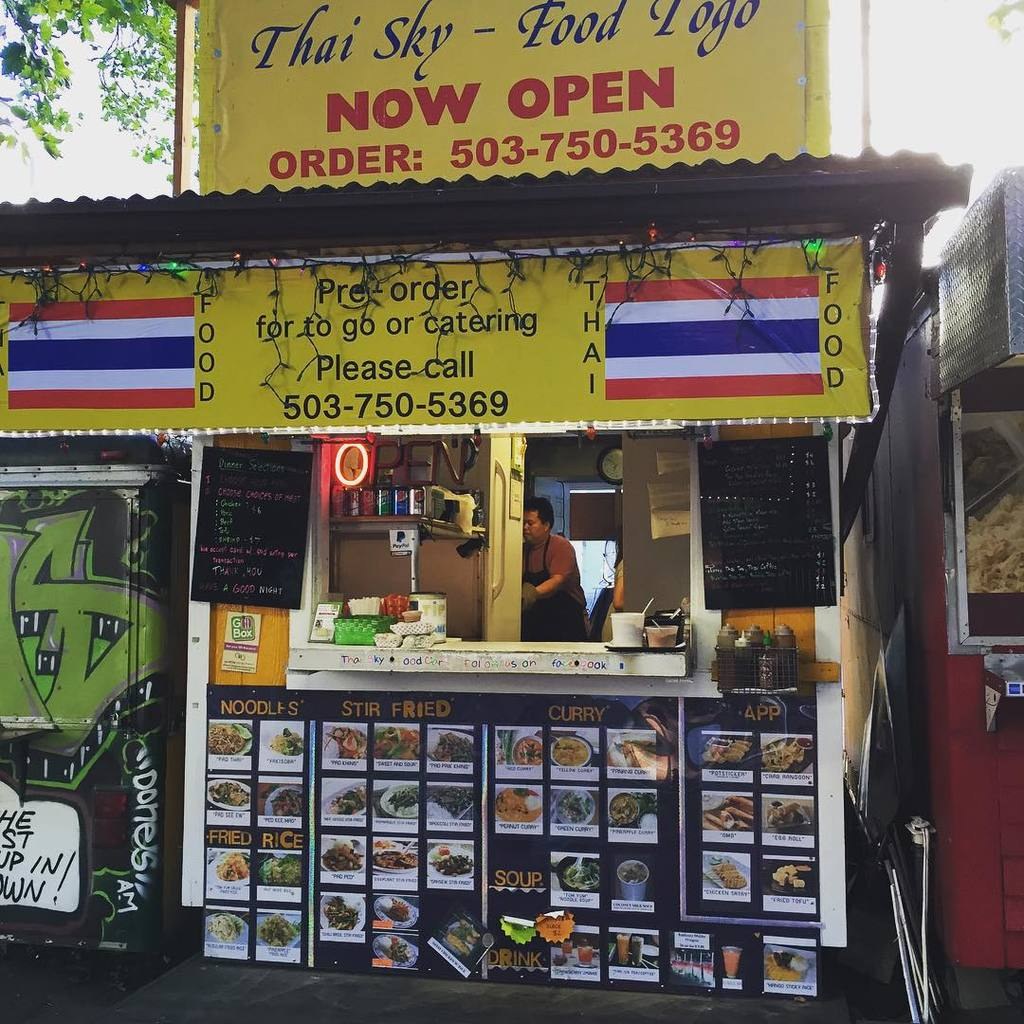 Läden, Getränkedosen, Speisekarten, eine Uhr, Gewürze in Plastikbehältern, Kondimente, Werbetafeln, Namensschilder und Himmel.