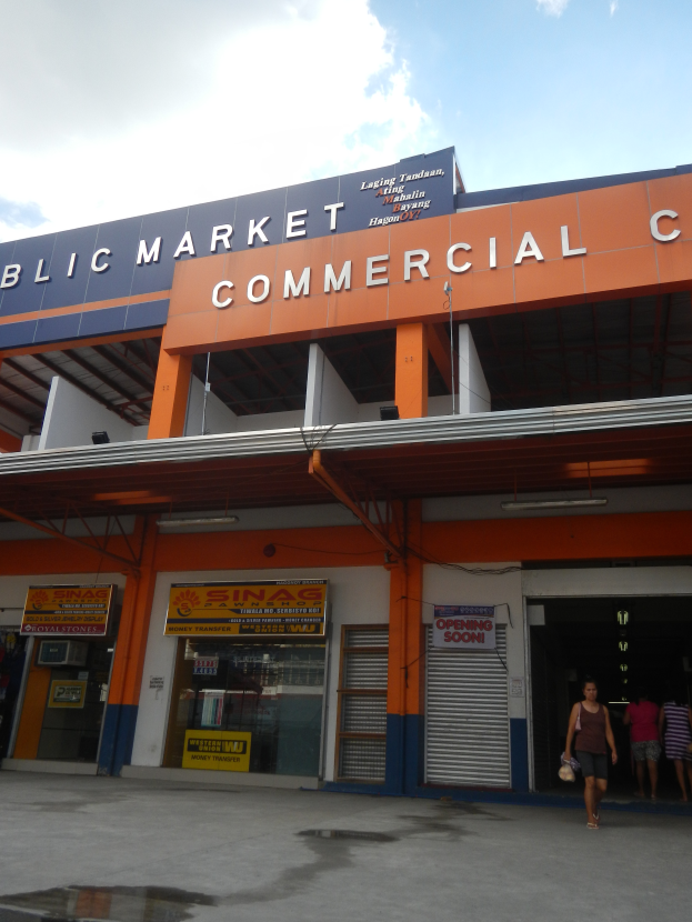 Ein öffentlicher Markt mit Menschen davor, Text auf dem Gebäude und ein sichtbarer Himmel oben.