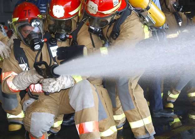 Feuerwehrleute in Schutzausrüstung sprühen Wasser auf einen Boden in der Nähe einer Wand.
