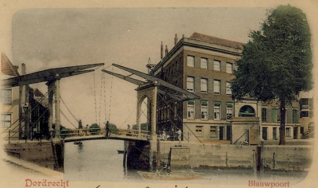 Altes Schwarz-Weiß-Foto einer Brücke unter construction, die einen Fluss überspannt, mit Gebäuden, Bäumen und einem klaren Himmel im Hintergrund und verstreuten Baugeräten und Materialien am Boden.