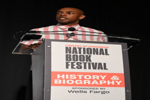 Ein Mann steht an einem Rednerpult mit einem Mikrofon und spricht bei einem Abendevent mit dem Titel "National Book Festival History & Biography."