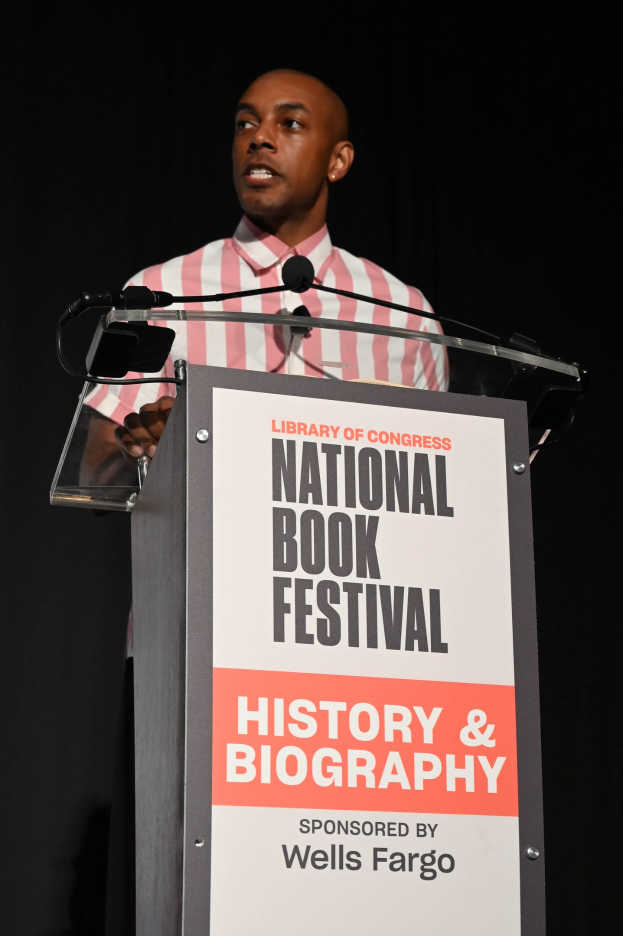 Ein Mann steht an einem Rednerpult mit einem Mikrofon und spricht bei einem Abendevent mit dem Titel "National Book Festival History & Biography."