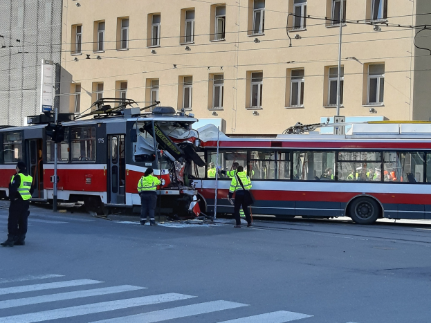 Eine rote und weiße Straßenbahn, die in einen Unfall auf der Straße verwickelt ist, mit einigen Menschen in der Nähe und einem Gebäude im Hintergrund.