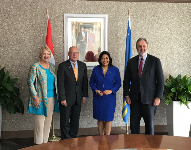 Eine Gruppe strahlender Menschen um einen Tisch mit Papieren stehend, umgeben von Fahnen, Topfpflanzen und einem Foto auf der Wand, feiert die Unterzeichnung eines Memorandums zwischen den Vereinigten Staaten und Kanada.