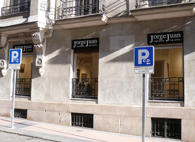 Ein mehrgeschossiges Gebäude mit Fenstern, Geländern, Türen und Säulen, das Werbetafeln auf Pfählen entlang des Gehwegs und sichtbare Innenobjekte zeigt, die auf eine belebte städtische Umgebung hinweisen.