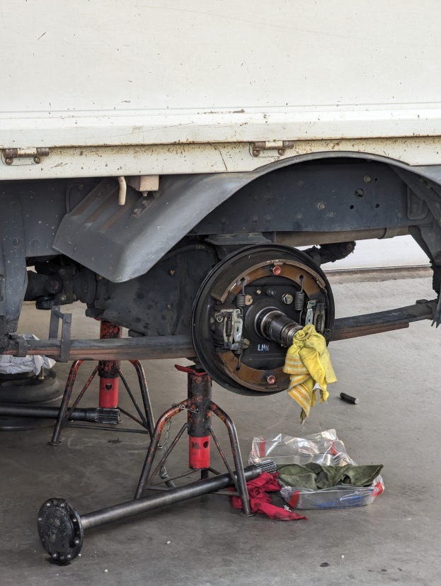 Ein gelber, mit einem Tuch bedeckter Lastwagen in einer Garage mit Werkzeugen und Gegenständen, die vor ihm auf dem Boden verstreut sind.