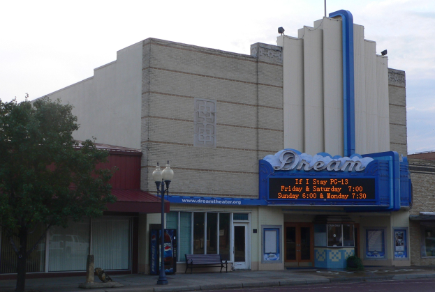Dream Theater an einer Straßenecke mit umliegenden Gebäuden, Straßenlaternen, einer Bank, einem Baum und einem wolkenverhangenen Himmel.