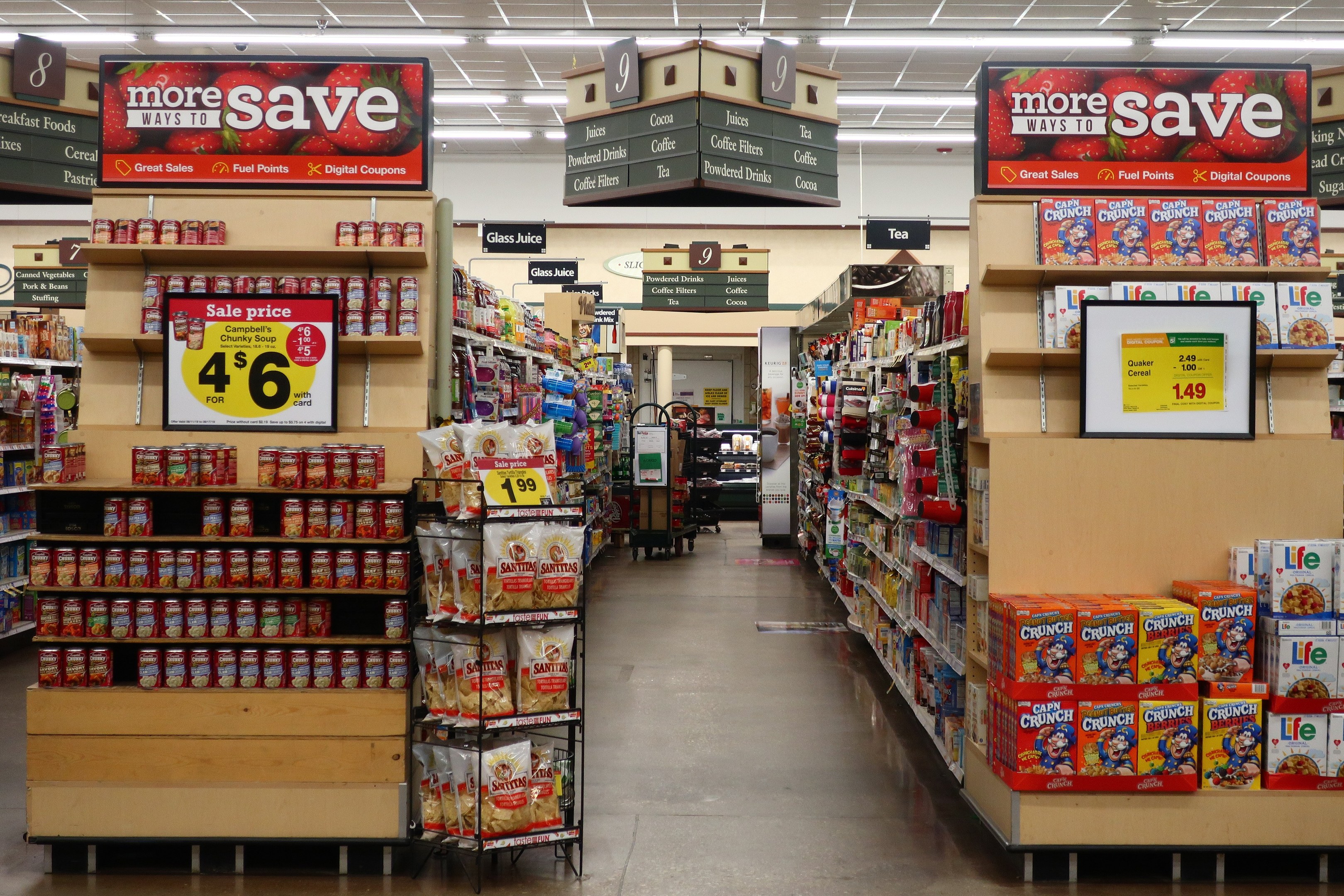 Ein Kiosk-Interieur Mit Regalen Und Boden, Bestückt Mit Verschiedenen Lebensmitteln, Beleuchtet Durch Deckeneinbauleuchten, Featuring Informations-Boards Und Eine Person Im Hintergrund.