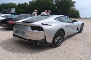 Roter Ferrari 812 Superfast bei der Goodwood Festival of Speed, umgeben von Zuschauern mit Mützen und Veranstaltungsbeschilderung im Hintergrund.
