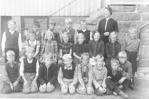 Schwarz-weiß-Foto einer Gruppe von Kindern, die vor einem Gebäude mit einer Wand, Treppen mit Geländern und der Aufschrift "1930er Schulkinder" am unteren Rand posieren