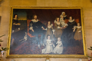 Gemälde einer Familie in einem Raum mit einem Weihnachtsbaum im Hintergrund, gerahmt und an der Wand gehängt mit zwei Fotorahmen auf beiden Seiten und dekorativen Gegenständen unten.