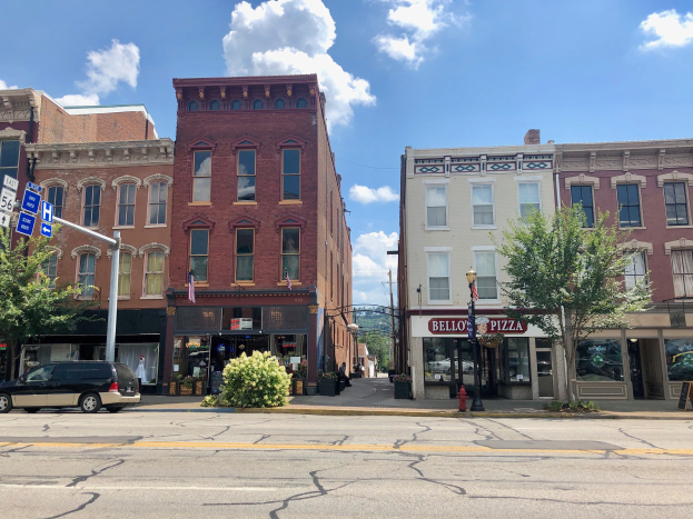 Eine Straße in einer Stadt mit parkenden Autos, Gebäuden, Bäumen, Laternenmästen, Schildern und einem Feuerhydranten unter einem bewölktem Himmel, die eine kommerzielle Immobilie für den Verkauf darstellt.