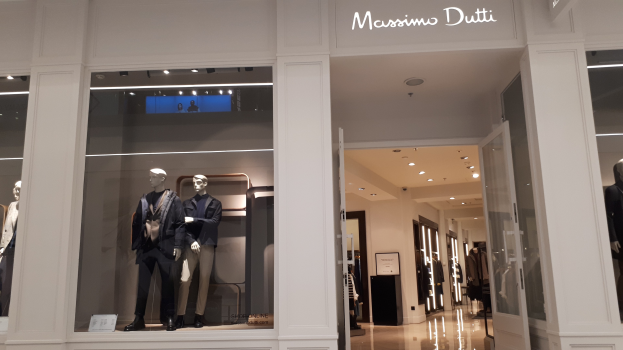 Innenansicht des Massimo Dutti Geschäfts in Mailand mit Schaufensterpuppen in aktueller Mode, Deckenbeleuchtung, Informationsschildern und Türen mit sichtbarem Boden.