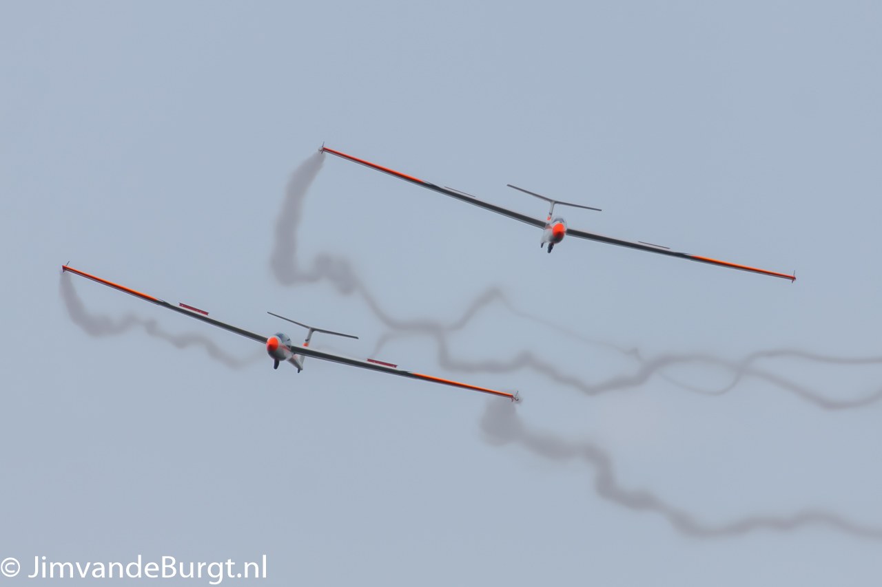 Zwei Segelflugzeuge mit Rauchspuren am Himmel, Text in der linken unteren Ecke.