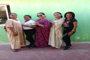 Eine Gruppe von Frauen steht zusammen vor einer grünen Wand mit einem Fenster auf der linken Seite und nimmt an einer Internationalen Frauentagsveranstaltung teil.