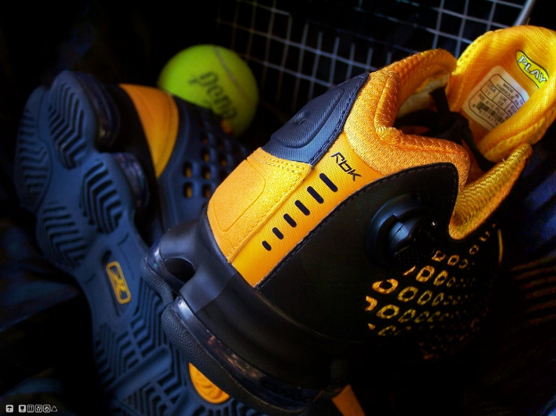 Ein Paar Schuhe und ein Ball befinden sich in der Mitte des Bildes, mit einem Zaun im Hintergrund.