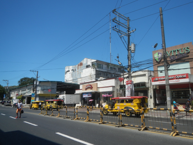 Eine belebte Stadtstraße mit Fahrzeugen, Fußgängern, hohen Gebäuden und einem klaren blauen Himmel.