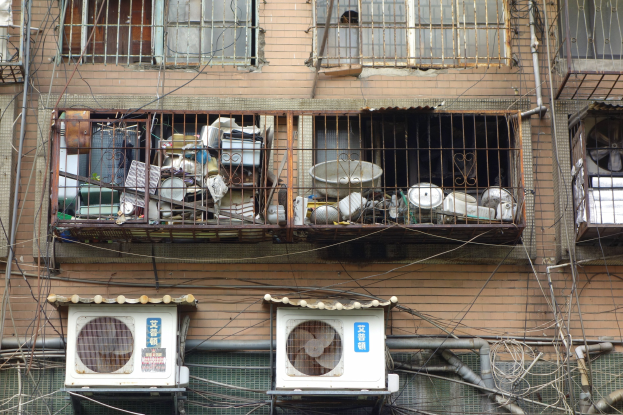 Wohngebäude mit Fenstern, Eisengittern, Klimaanlagen, Rohren und Kabeln an seiner Außenseite.