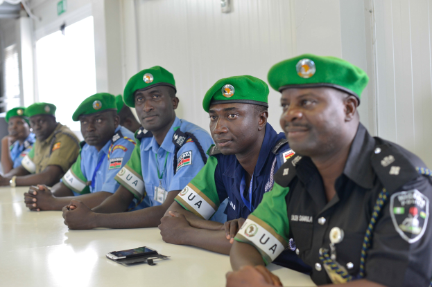 Gruppe von Polizeibeamten sitzt an einem Tisch mit Mobiltelefonen und anderen Gegenständen während einer Schulung in einem Raum mit Fenstern und Deckenleuchten.