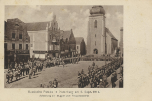 Ein Schwarz-Weiß-Foto eines Umzugs in Insterburg am 5. September 1914 mit vielen Menschen, Gebäuden im Hintergrund und Text am unteren Rand des Bildes.