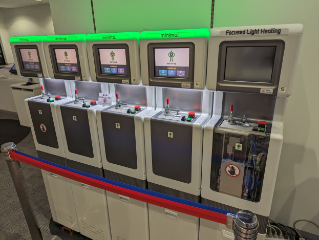 Eine Reihe von Mini-Heizungssystemgeräten mit Steuerknöpfen und -rädchen, die in einem Raum mit einer Wand, Deckenleuchten und einem Boden aufgereiht sind.