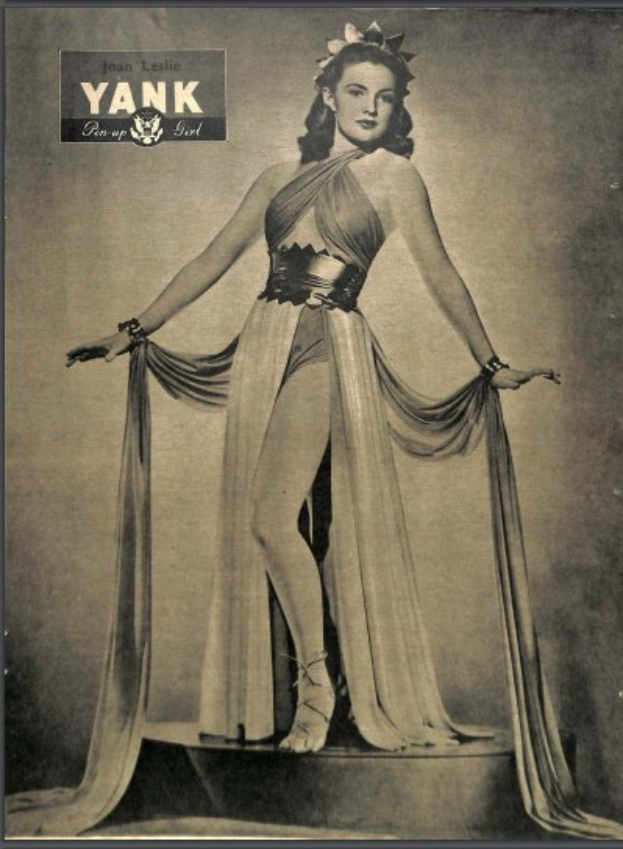 Ein Schwarz-Weiß-Foto von Schauspielerin Joan Leslie in einem langen, hochgeschlossenen Kleid mit langen Ärmeln, die selbstbewusst auf einer Bühne steht, mit geschlossenen Augen, eingerahmt von dem Text "Joan Leslie" oben.