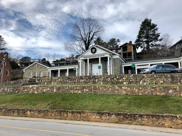 Steinwand mit geparkten Autos, angrenzende Gebäude mit Fenstern und Türen, Bäume und ein bewölkter Himmel im Hintergrund, als Weltkulturerbe-Museum bezeichnet.