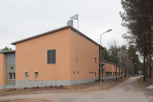 Ein orangefarbenes Gebäude mit einer Flagge auf dem Dach, umgeben von Laternenmästen, Straßenlaternen, Kraftfahrzeugen, Bäumen und einem klaren blauen Himmel.