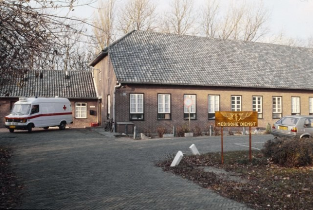 Ambulanz vor einem Backsteingebäude mit Fenstern, einem Schild, Grünfläche und einem klaren blauen Himmel geparkt