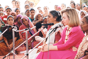 Eine Gruppe von Frauen sitzt auf dem Boden an einem öffentlichen Ort, jede hält ein Mikrofon und unterhält sich mit einer Menge im Hintergrund.