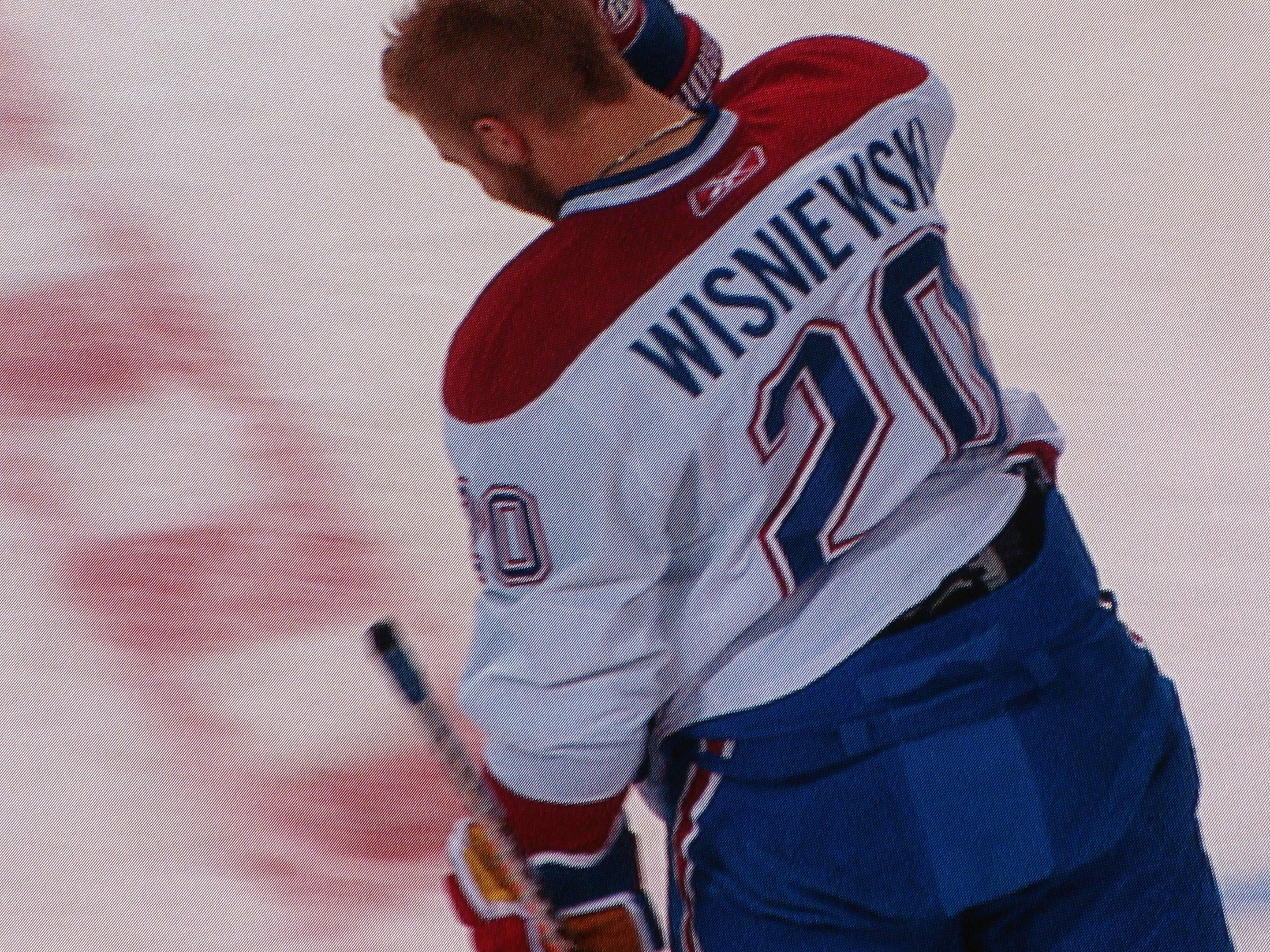 Ein Hockey-Spieler in einem "Wisniewski"-Trikot steht auf dem Eis und hält einen Hockey-Schläger, mit einem konzentrierten und entschlossenen Gesichtsausdruck.