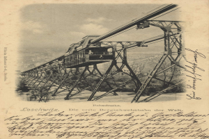 Ein altes Schwarz-Weiß-Foto einer Eisenbahnbrücke mit einem Kran, umgeben von Bäumen und einem bewölkten Himmel, mit Text unten lesbar "Bahnstrecka, die erste Eisenbahnbrücke in Deutschland".