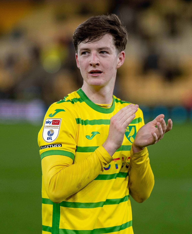 Ein junger Mann in einem gelb-grünen T-Shirt klatscht auf einem Fußballfeld, während er feiert, mit einem unscharfen Hintergrund, der seine freudige Reaktion betont.
